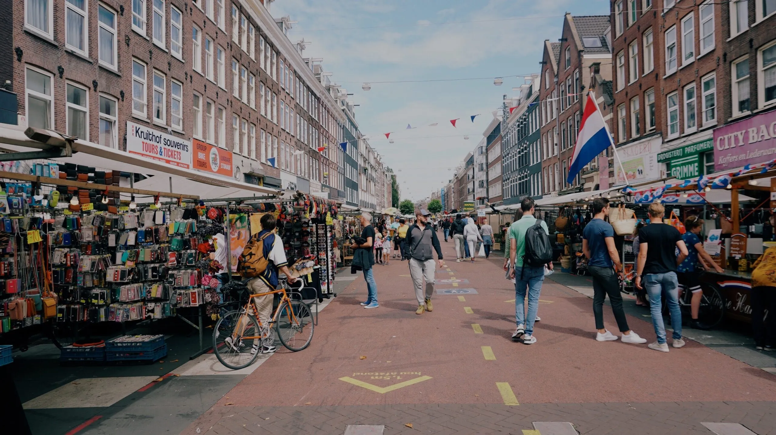 A busy Amsterdam street market with Dutch flags overhead
