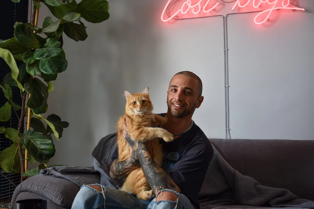 Portrait of a man holding a ginger cat under a neon sign